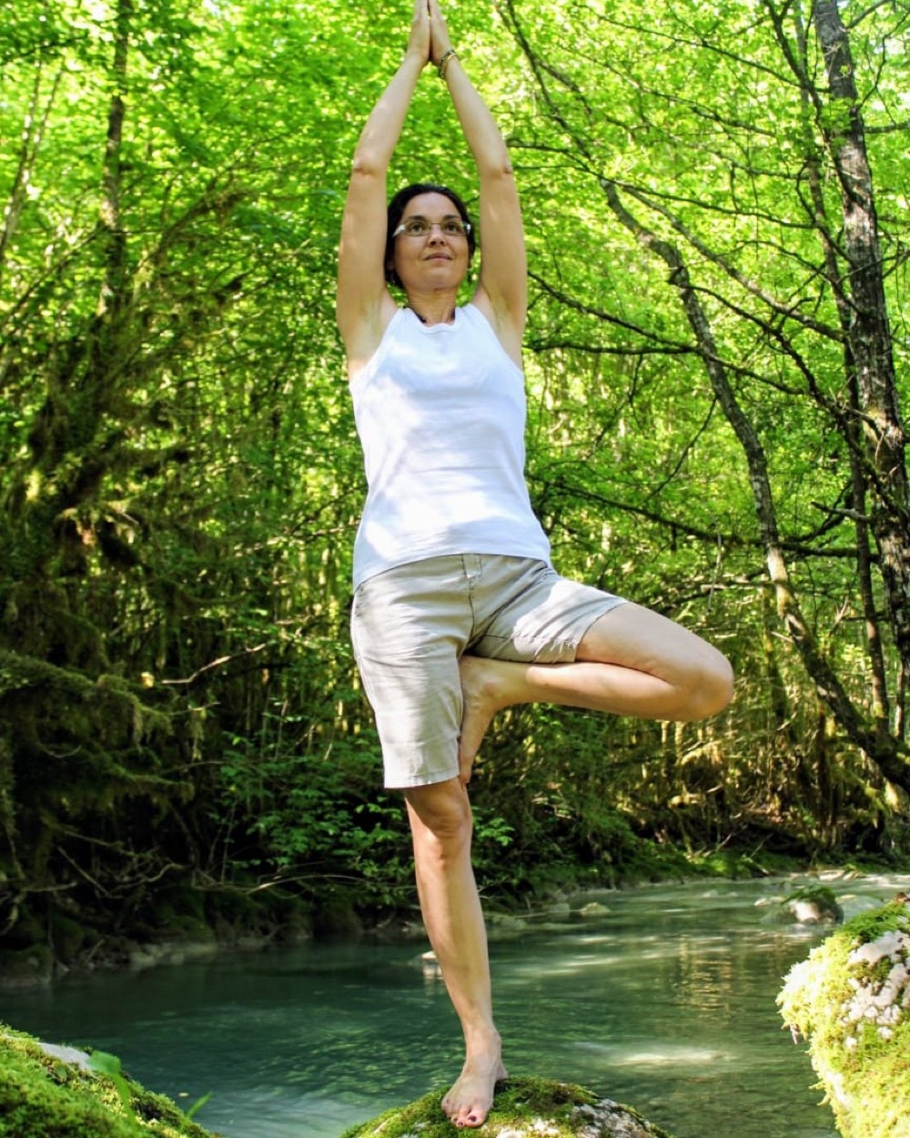 Posture de l'arbre (yoga) pratiquée en pleine nature, au bord d'un ruisseau